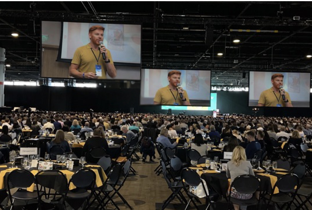 Lipe Camanzano palestrado em evento com milhares de participantes, projetado em telões gigantes