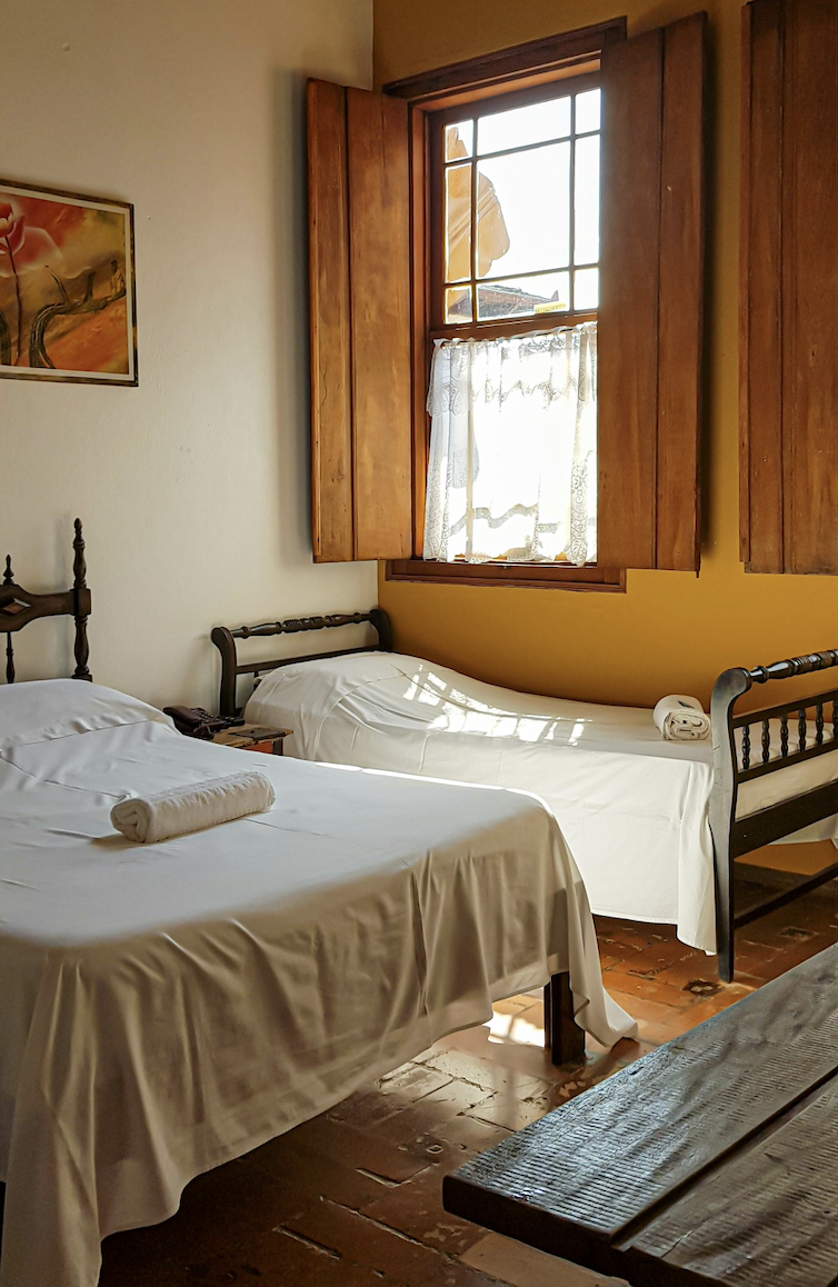 Quarto de hotel simples e acolhedor com cama, janela e luz natural